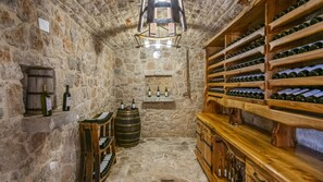 A stone-walled cellar with wooden racks of wine bottles, a barrel, and a wooden bench. - Villa Mia by Villas Guide (Krivodol)