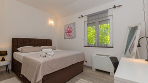 A bedroom with a large bed, a bedside table with a lamp, a radiator, and a window with blinds.