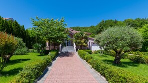 A pathway leading to a building with a red-brick entrance, surrounded by lush greenery and trees.