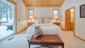 A bedroom with a large bed, wooden ceiling, two bedside tables with lamps, a bench, and a door leading to a bathroom. - Pinewood Lodge by AvantStay | Cozy Cabin Near Ski Resorts & Hiking (Truckee)