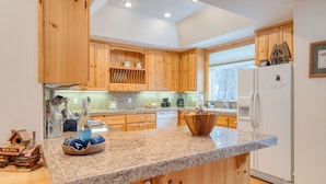 A modern kitchen with wooden cabinets, granite countertops, and a central island with a bowl of fruit. - Pinewood Lodge by AvantStay | Cozy Cabin Near Ski Resorts & Hiking (Truckee)