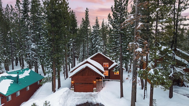 A cabin with a green roof, surrounded by tall pine trees and covered in snow. - Pinewood Lodge by AvantStay | Cozy Cabin Near Ski Resorts & Hiking (Truckee)