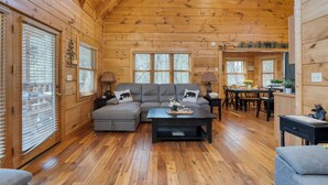 Un accogliente interno di una baita con pareti in legno, un divano componibile, un'area pranzo e ampie finestre.