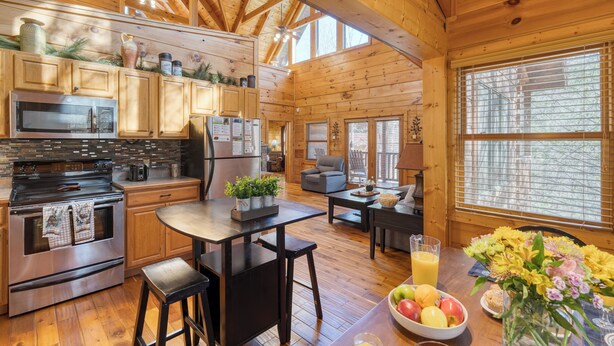 Un'ampia baita in legno con una cucina dotata di elettrodomestici moderni, un'area pranzo con tavolo e sedie e ampie finestre che offrono luce naturale.