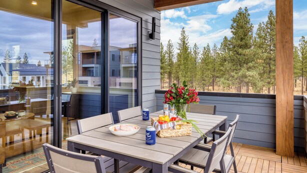 A wooden deck with a table set for dining, a vase with flowers, and a view of trees and buildings in the background.
