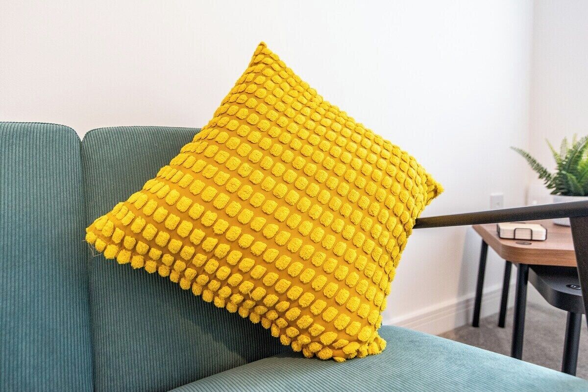A green sofa with a yellow textured pillow.