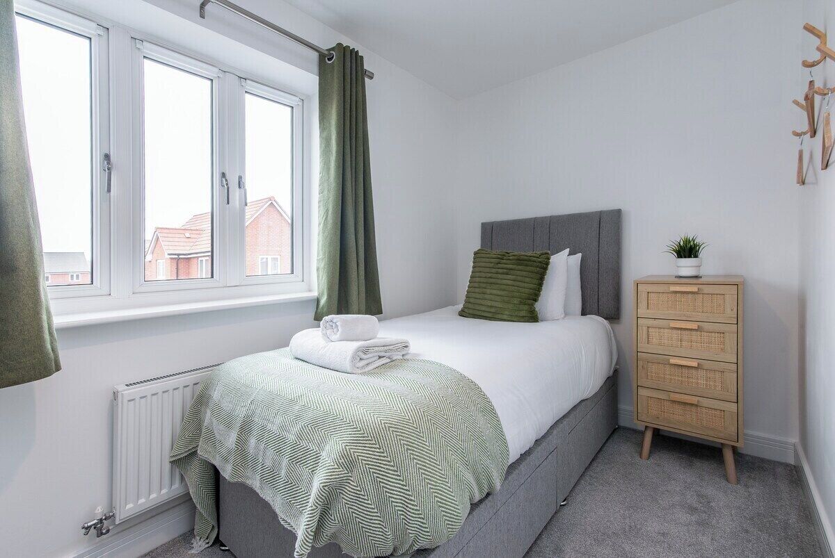 Une chambre à coucher avec un lit, un radiateur, une fenêtre avec des rideaux, une commode et une plante.