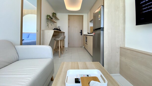 A modern hotel room with a sofa, a small dining table, a kitchen area with a refrigerator, and a TV displaying a menu. - Fantasea Condo Kamala (Kamala)
