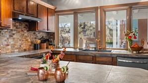 Una cucina moderna con mobili in legno, zoccolo in pietra e ampie finestre con vista sugli alberi.