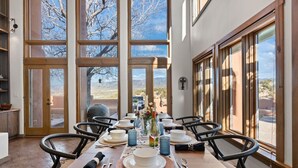 Zona pranzo con tavolo apparecchiato per sei persone, ampie finestre e vista su un paesaggio desertico.