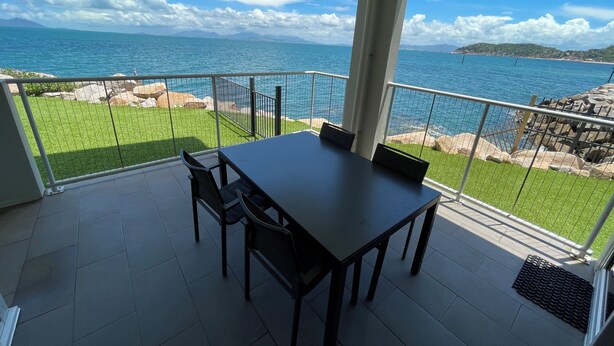 Un balcón con mesa y sillas, con vista al mar y rocas a la costa.