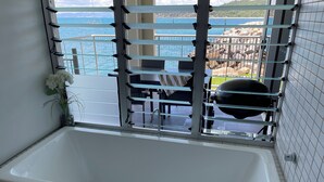 Un baño con bañera, una ventana con barrotes y vista al mar.
