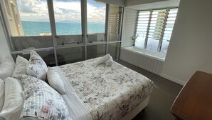 Un dormitorio con una cama grande, vistas al mar a través de ventanas de techo a suelo y una bañera junto a la ventana.