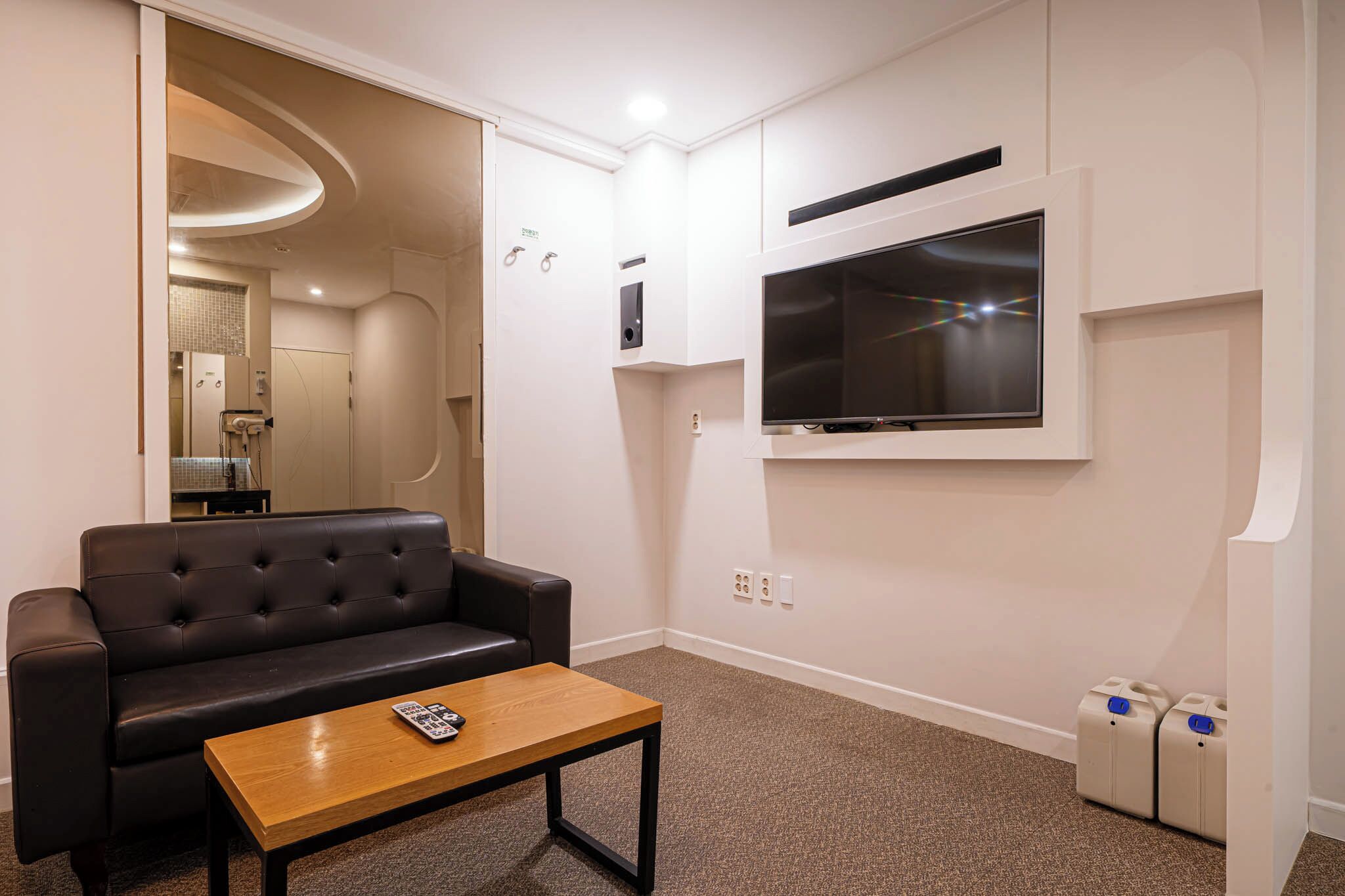 A modern living room with a leather sofa, a wooden coffee table, a flat-screen TV mounted on the wall, and a built-in sound system.