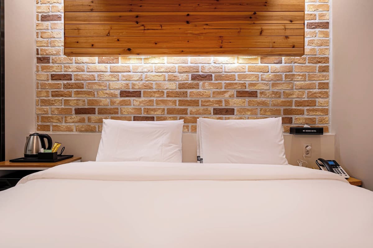 Une chambre d’hôtel avec un mur en briques, un plafond en bois et un lit recouvert de draps blancs.