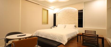A modern bedroom with a large bed, a bedside table, a chair, and a small table.