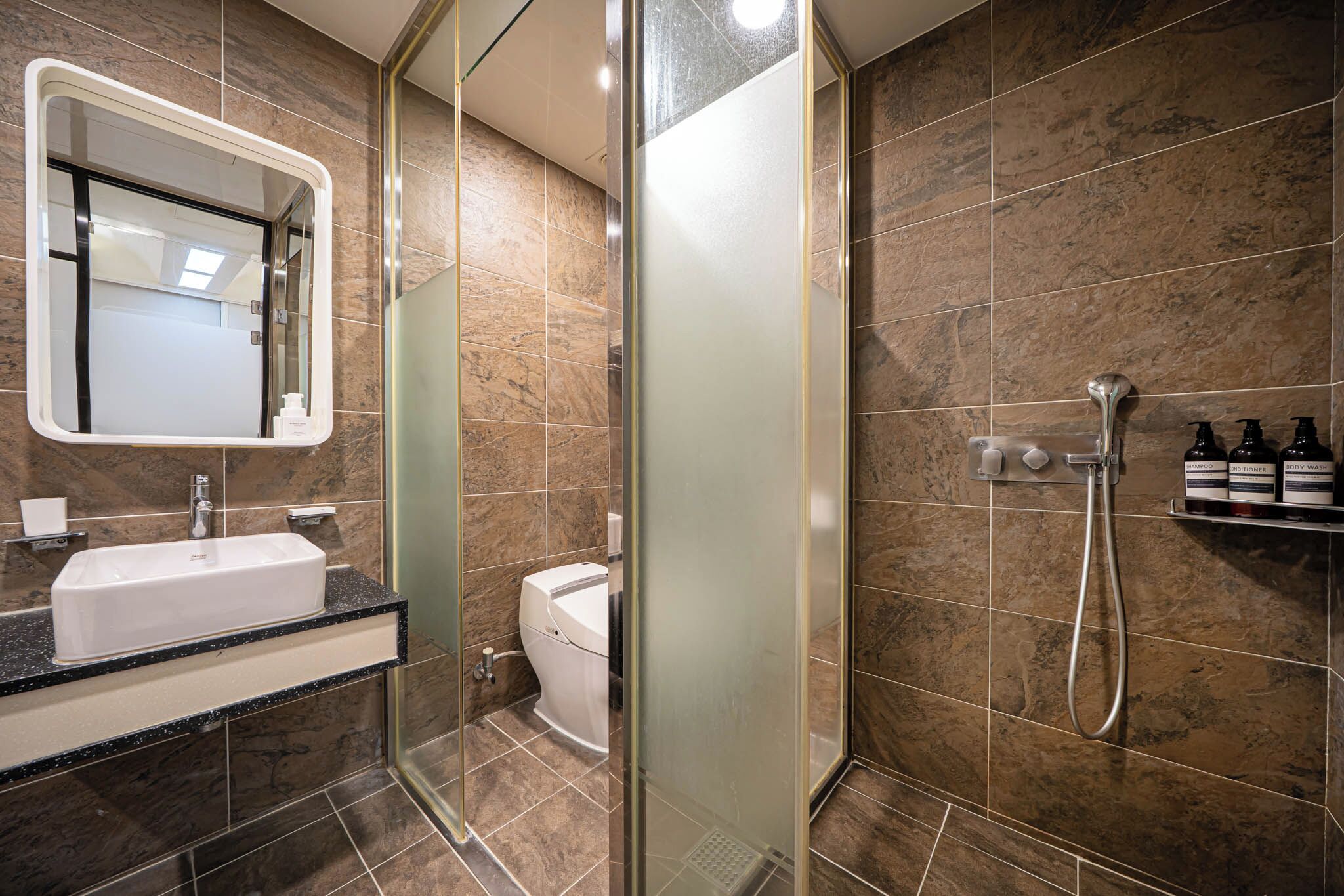 A modern bathroom with a glass-enclosed shower, a white sink, and a marble-tiled wall.