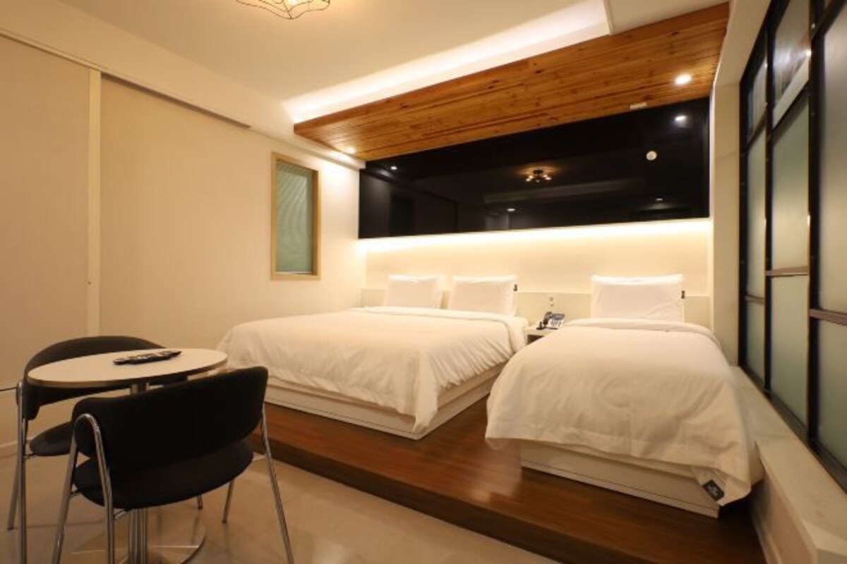 A modern hotel room with two beds, a small round table, and a chair.