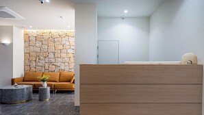 Ein moderner Empfangsbereich mit einer Steinwand, einem Holzbüro, einer Couch und zwei Mustertischen.