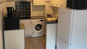 A compact kitchen with white cabinets, a washing machine, a microwave, and a refrigerator.