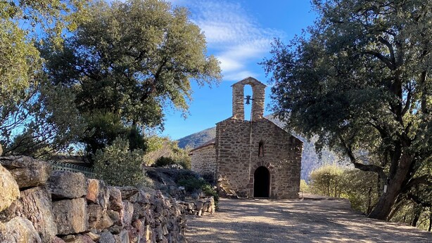 A stone church with a bell tower, surrounded by trees and a stone wall.