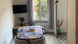 A compact living space with a dining table, two chairs, a TV, and a window with curtains.
