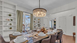 A dining area with a long table set for six, surrounded by shelves with decorative items. - LuxEscape | HotTub+Sauna, GameRm, Firepit, Playset (Overland Park)
