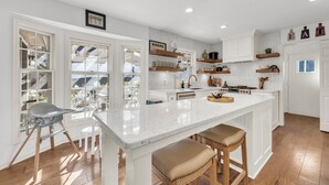 A spacious kitchen with a large island, white cabinetry, and wooden shelves. - LuxEscape | HotTub+Sauna, GameRm, Firepit, Playset (Overland Park)
