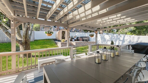 An outdoor patio with a pergola, a dining table with chairs, hanging lanterns, and a grill area. - LuxEscape | HotTub+Sauna, GameRm, Firepit, Playset (Overland Park)