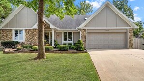 A two-story house with a stone facade, a garage, and a well-maintained lawn. - LuxEscape | HotTub+Sauna, GameRm, Firepit, Playset (Overland Park)