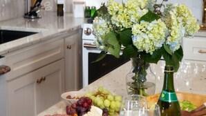 A kitchen counter with a variety of food items, a bottle of wine, and a vase of flowers. - LuxEscape | HotTub+Sauna, GameRm, Firepit, Playset (Overland Park)