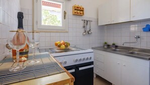 Eine Küche mit weißen Schränken, einem Herd, einer Spüle und einem Fenster mit Blick auf Grünfläche.
