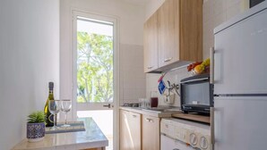 Een moderne keuken met houten kastjes, een ingebouwde wasmachine, een magnetron en een raam met uitzicht op bomen.
