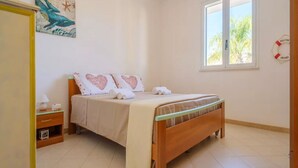 Een slaapkamer met een bed, een nachtkastje, een raam en een schilderij aan de muur.
