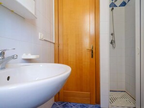 Une salle de bain avec une porte en bois, un lavabo blanc et un espace douche.