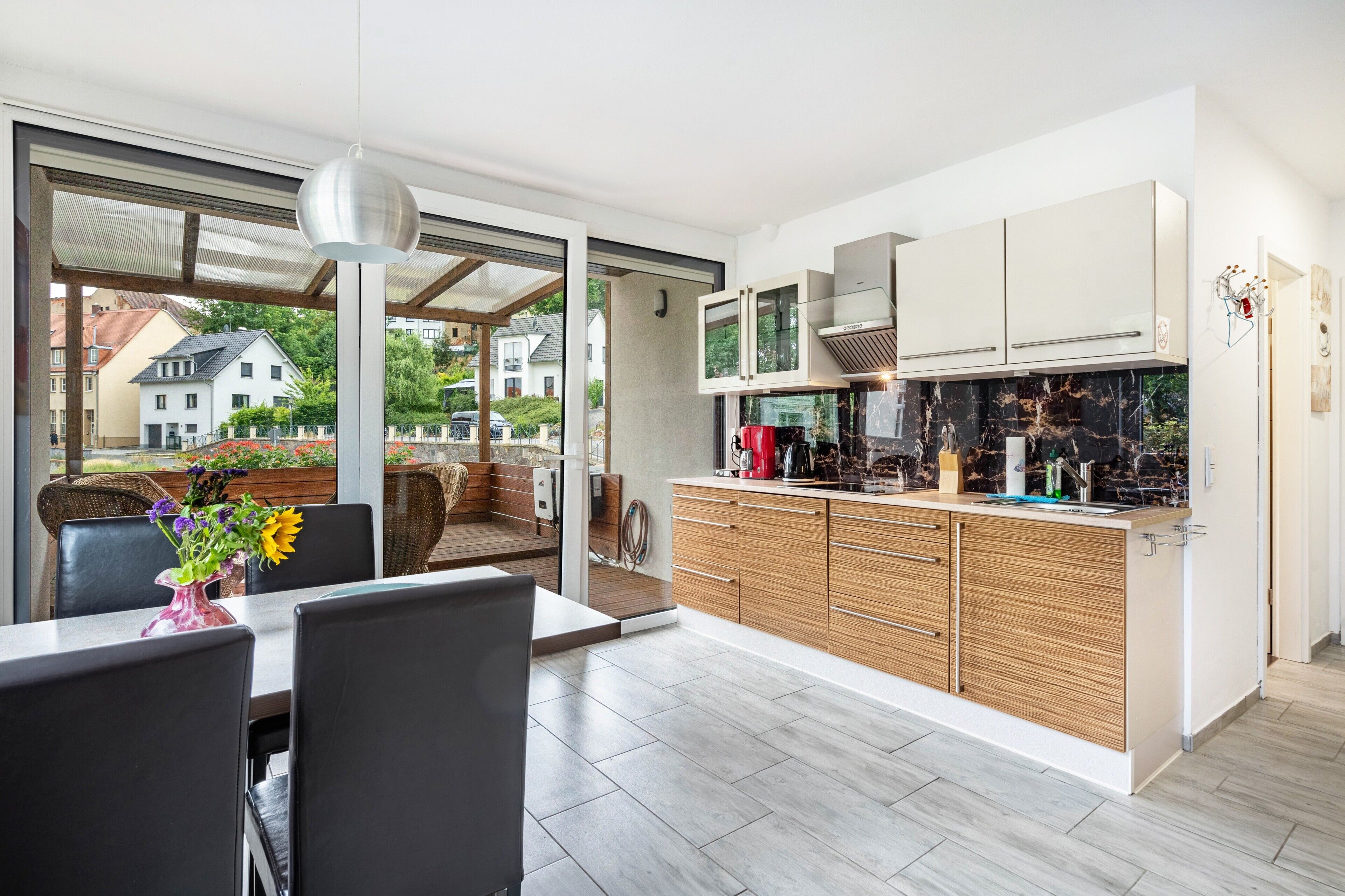 A modern kitchen with a large island, sliding doors leading to a balcony, and a dining area with a table and chairs.