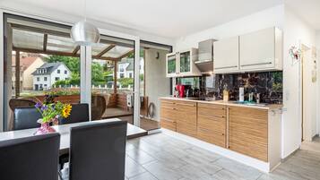 A modern kitchen with a large island, sliding doors leading to a balcony, and a dining area with a table and chairs.