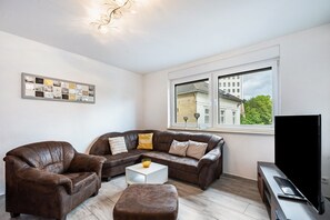 A living room with a sectional sofa, a coffee table, a TV, and a window with a view of buildings.