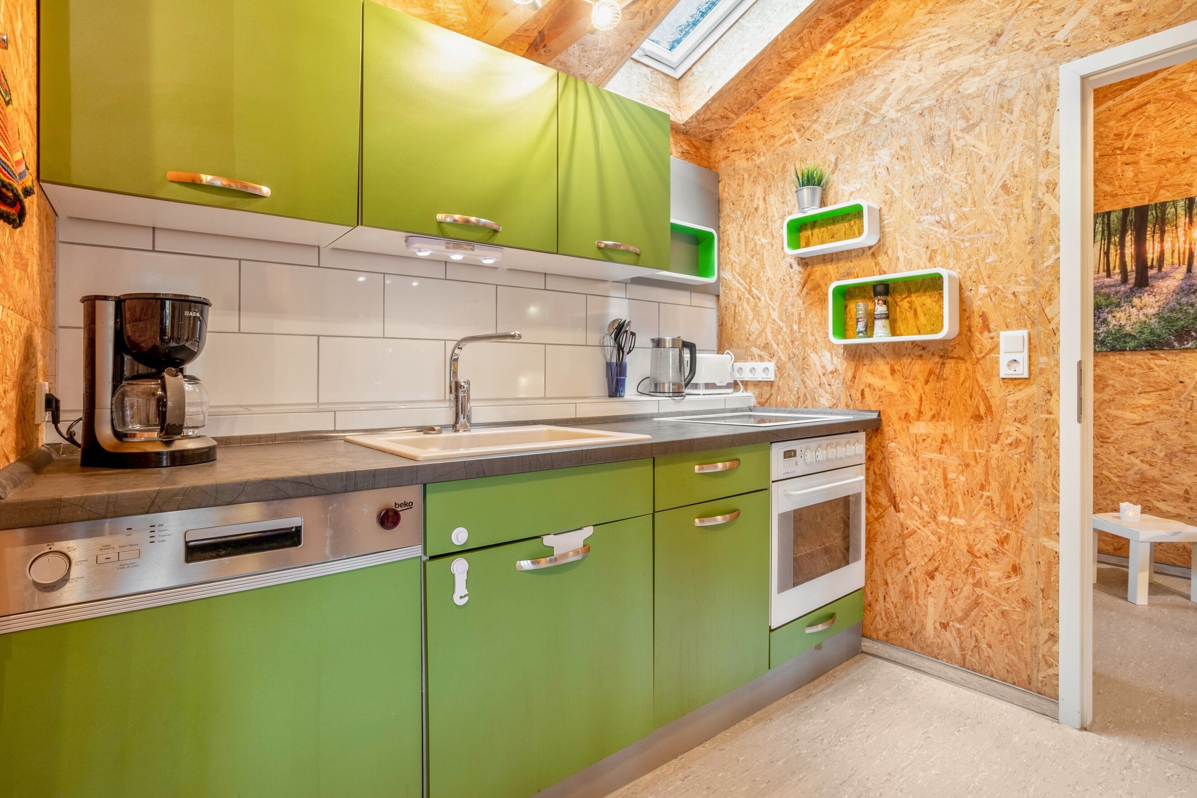 Une cuisine avec des meubles de couleur verte, une machine à café, un évier et une cuisinière.