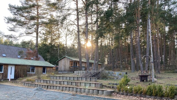 Una cabana rústica amb teulada verda, envoltada per un bosc.