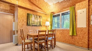 Habitació amb panells de fusta, una taula de dinar, cadires, un quadre, una finestra amb cortines i una porta.