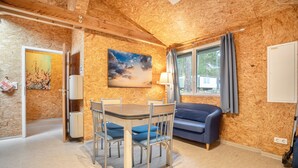 A room with a wooden ceiling, a dining table with chairs, a sofa, a window with curtains, and a painting on the wall.
