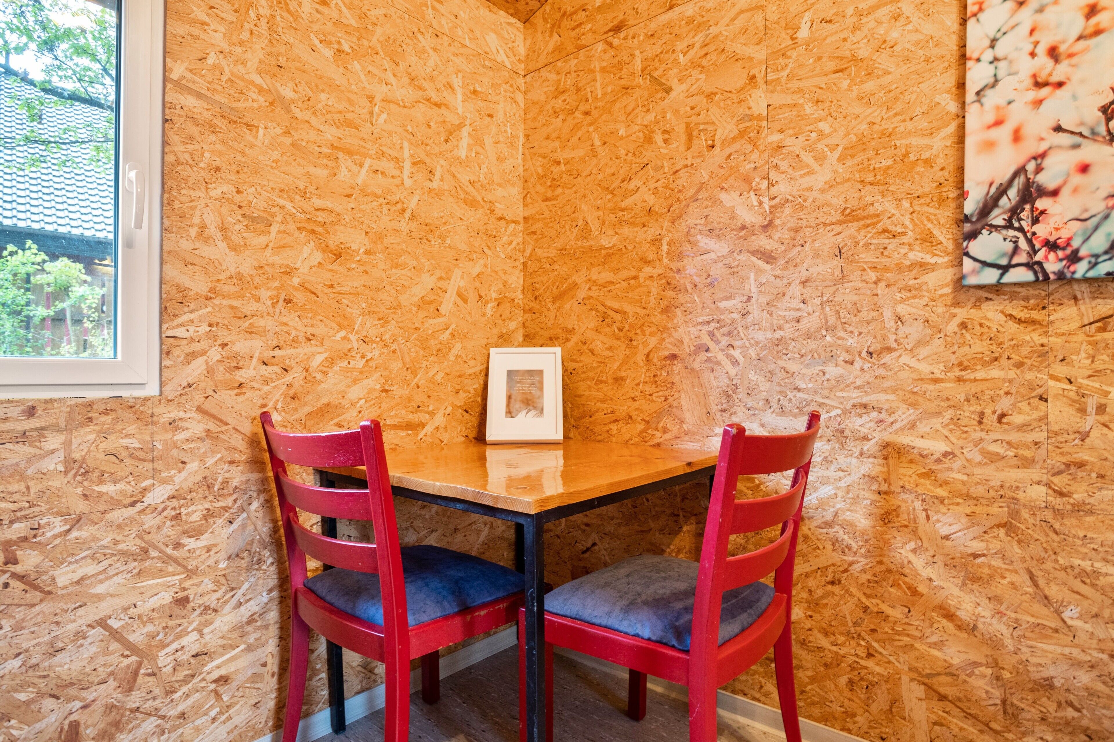 A corner room with a wooden wall, a window, and a framed picture on the table.