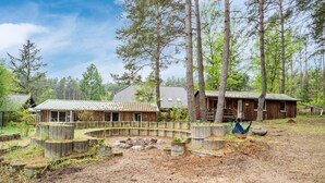 A rustic cabin with a curved wooden deck, surrounded by tall trees and a clear sky.