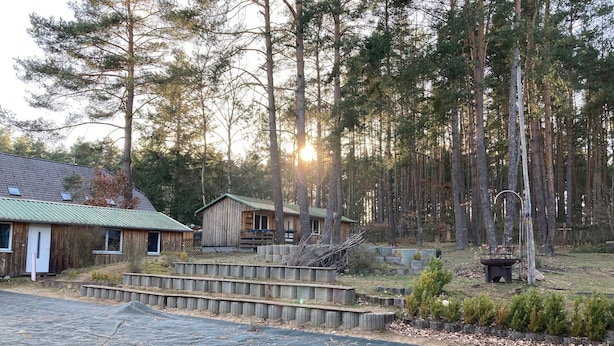 A rustic cabin with a green roof, surrounded by a forest.