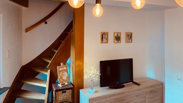 Un salon moderne avec un escalier en bois, un téléviseur à écran plat et des œuvres d’art décoratives accrochées au mur.