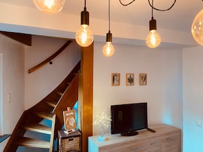 Una sala de estar moderna con una escalera de madera, un televisor de pantalla plana y decoración en las paredes.