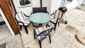 A patio with a round table and four chairs, a grill, and a window with a view. - Apartment 'Ella' with Mountain View, Private Terrace and Wi-Fi (Todtnau)