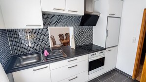 A compact kitchen with white cabinets, a black countertop, a stove, and a microwave. - Apartment 'Ella' with Mountain View, Private Terrace and Wi-Fi (Todtnau)