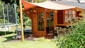 A wooden cabin with a covered patio, a trampoline, and a garden area.
